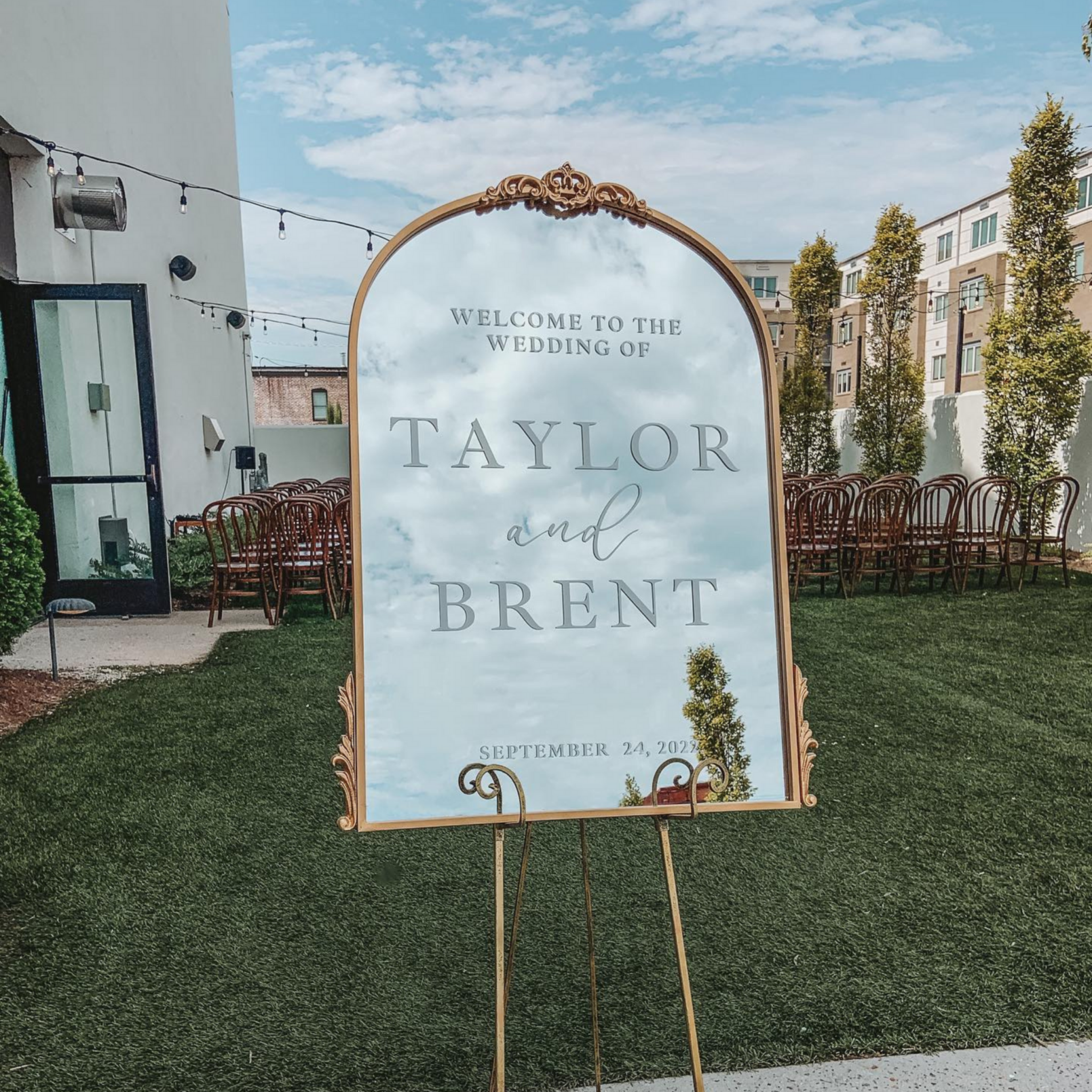 Antiqued gold arch wedding welcome sign with custom text at ceremony entrance.