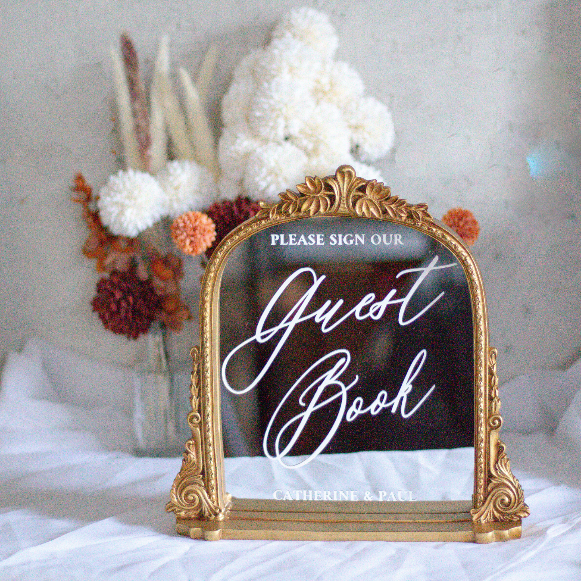 Elegant wedding guest book sign with calligraphy on a decorative mirror.