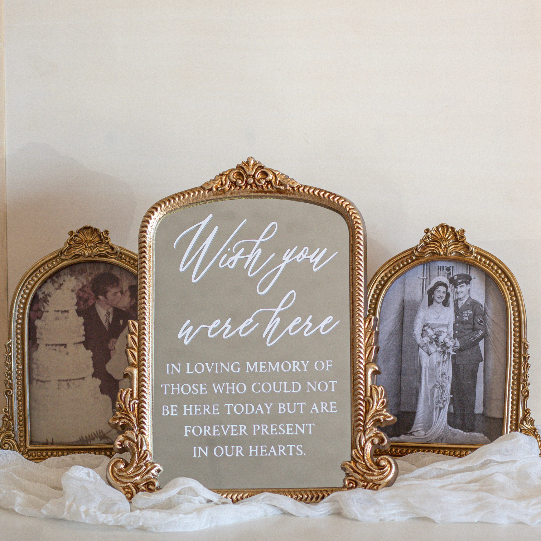 Wedding memorial sign with "Wish You Were Here" message on elegant mirror, surrounded by vintage photo frames.