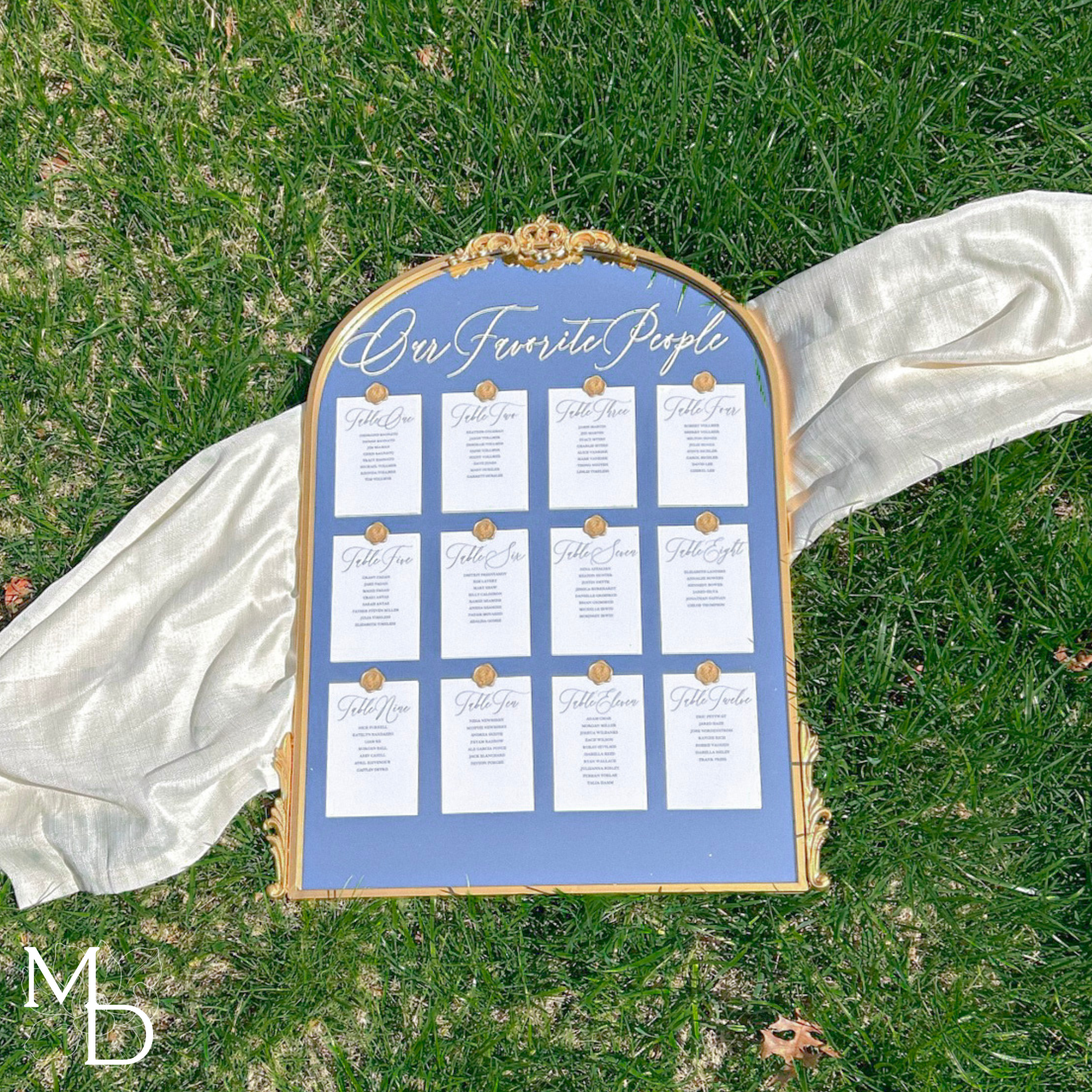 Wedding mirror seating chart with gold frame on grass, featuring customized wax seals and elegant calligraphy.