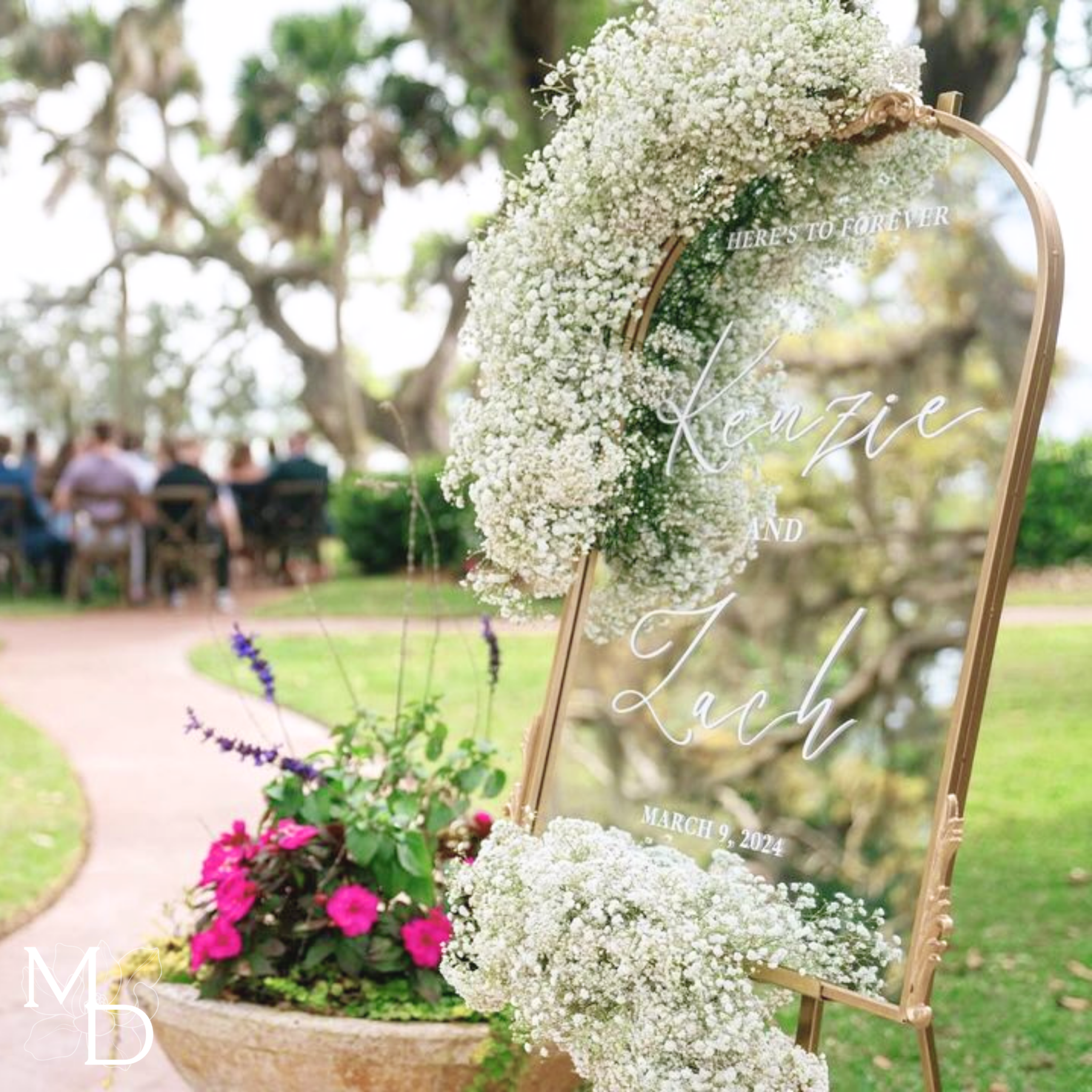 Elegant gold arch mirror wedding welcome sign with floral decoration at outdoor ceremony.