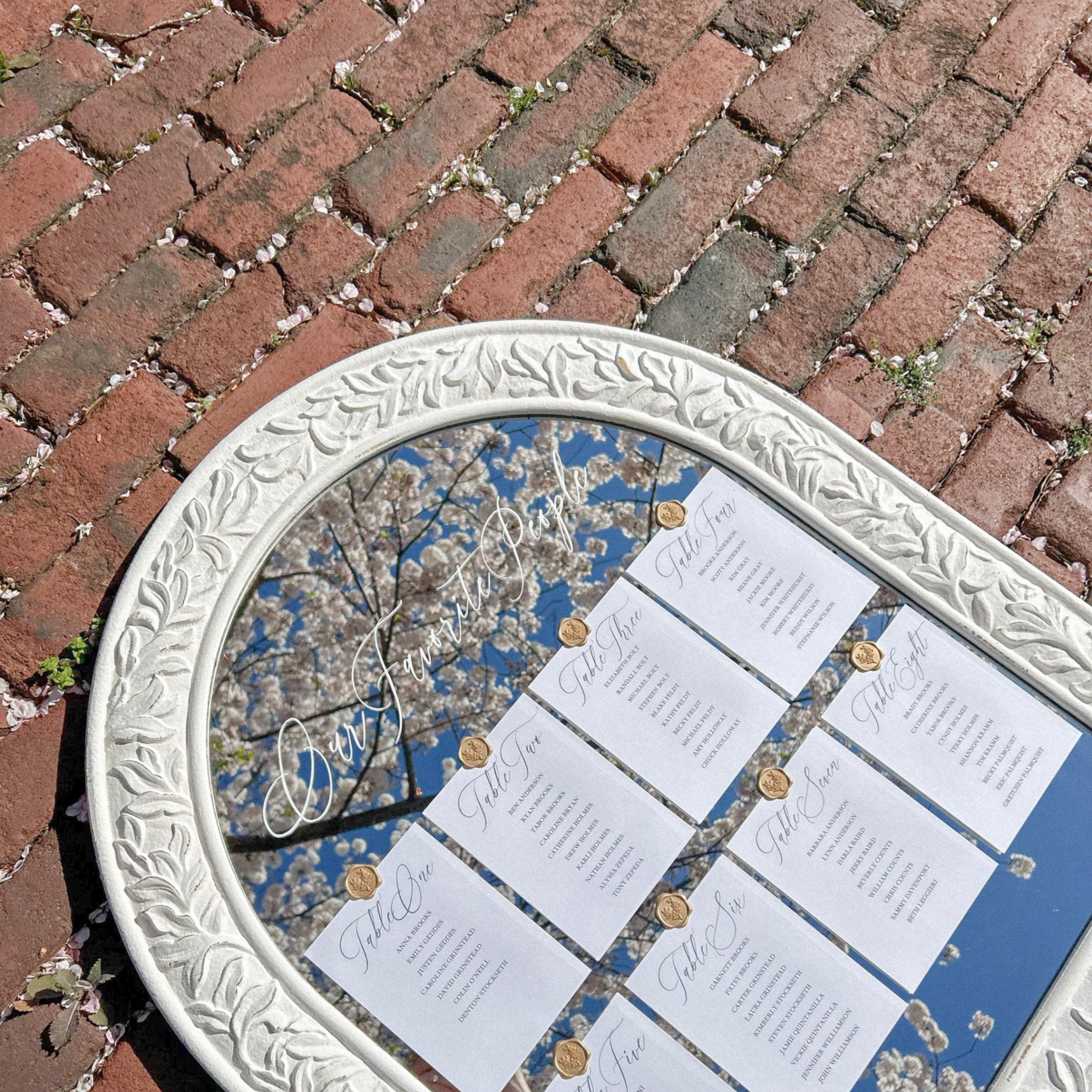 Wedding guest seating chart on a large white boho mirror with elegant name cards and gold wax seals.