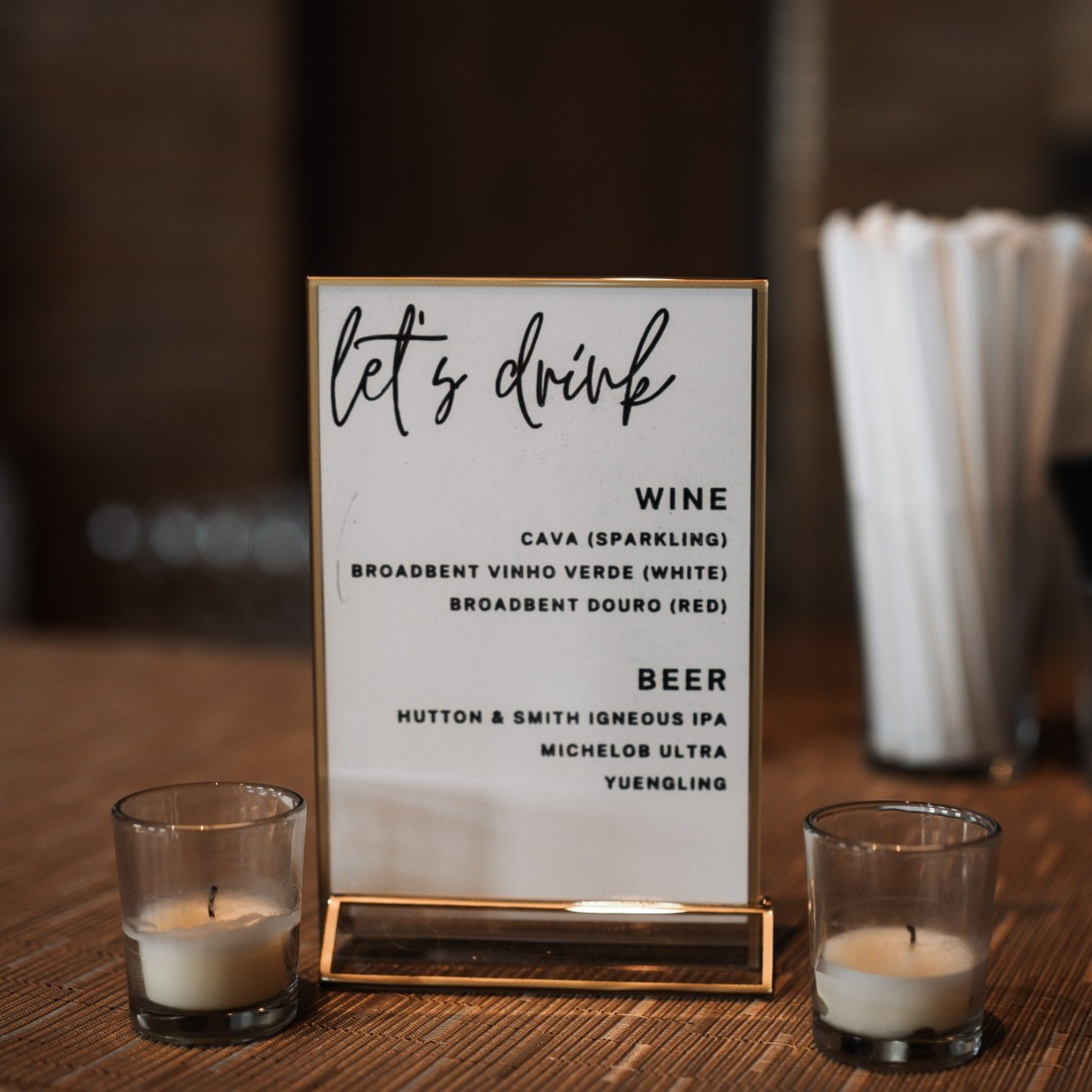 The Elizabeth Font on a Magnolia Dreams Custom Cocktail Menu for a Wedding Bar Set-Up on a gold frame with small tea candles beside it.