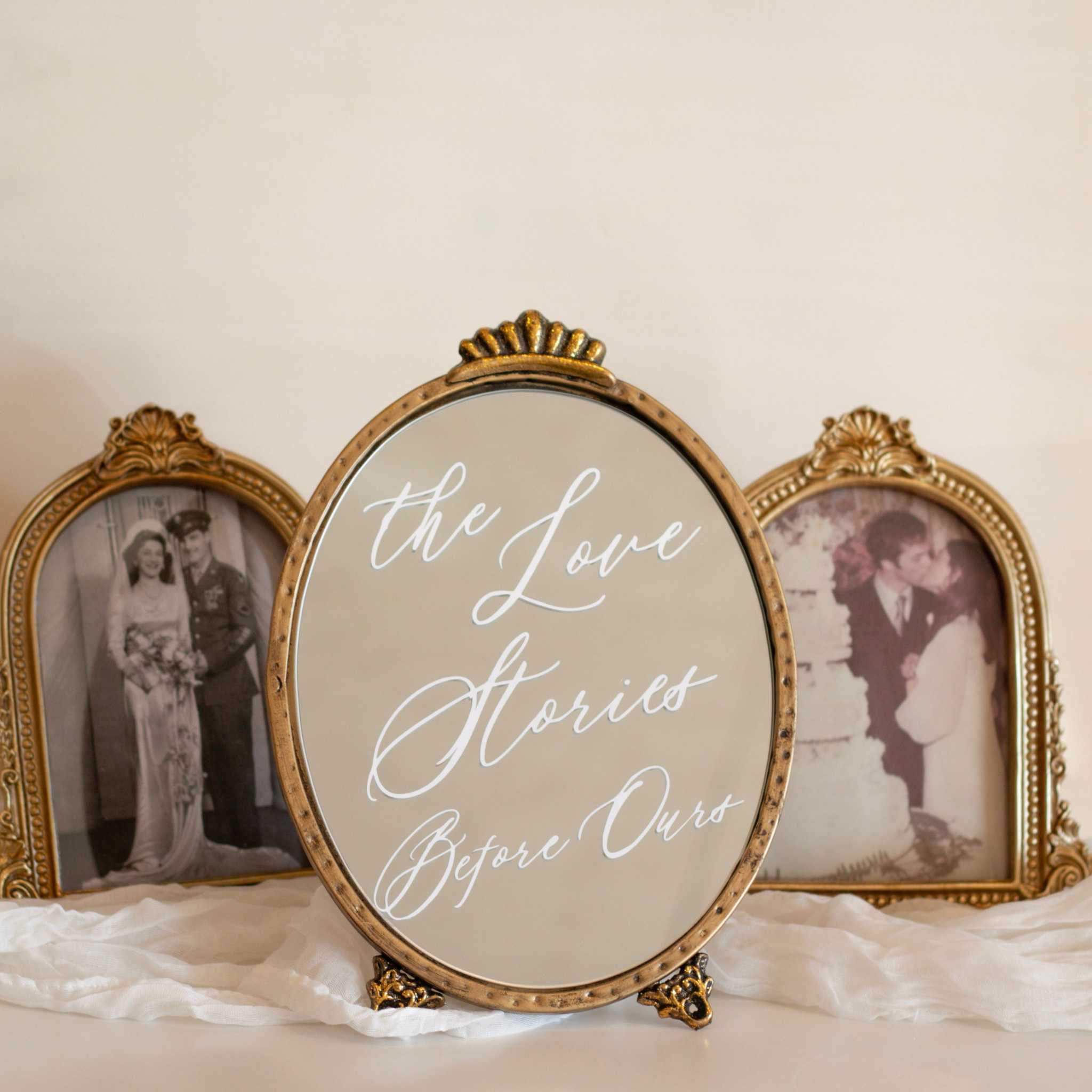 Generations of love wedding mirror sign featuring Love Stories Before Ours in white script on a vintage gold oval wedding mirror, styled on a cream chair with blush and ivory fabric, elegant wedding sign mirror decor for a remembrance table, honoring late parents, grandparents, and loved ones.