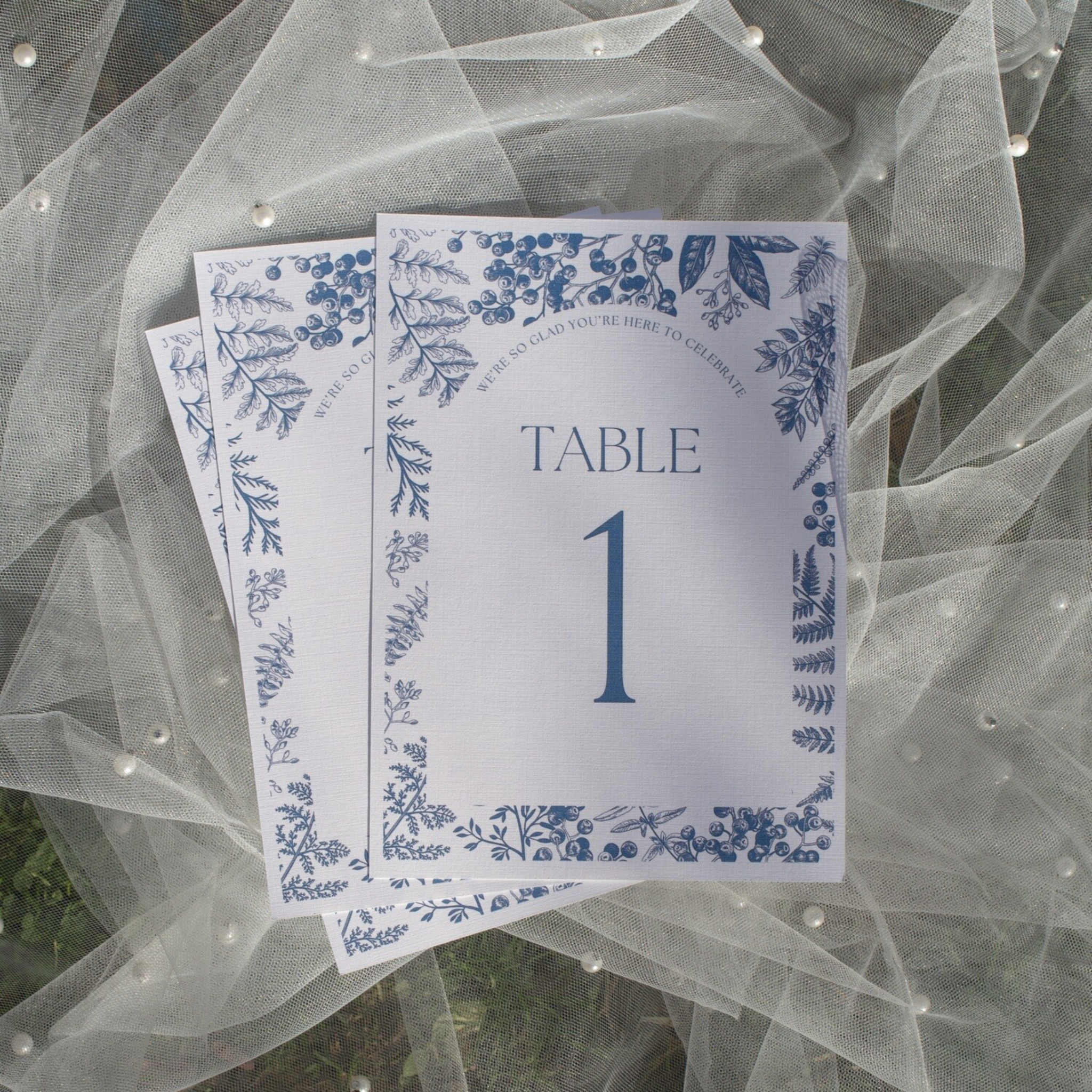 Blue and white wedding table numbers on luxury linen cardstock with floral border design.