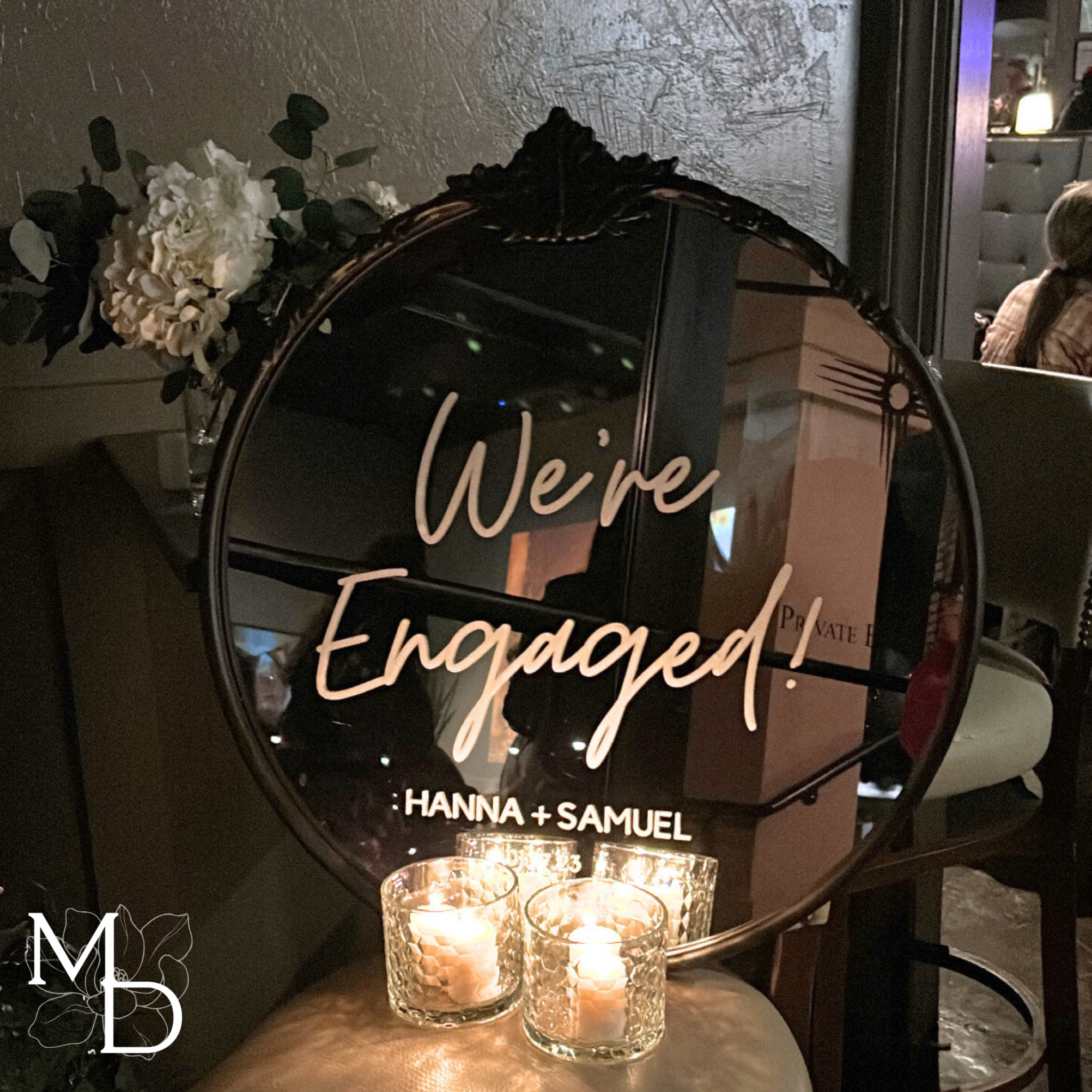 Ornate round engagement party welcome sign with personalized black mirror and gold accents.