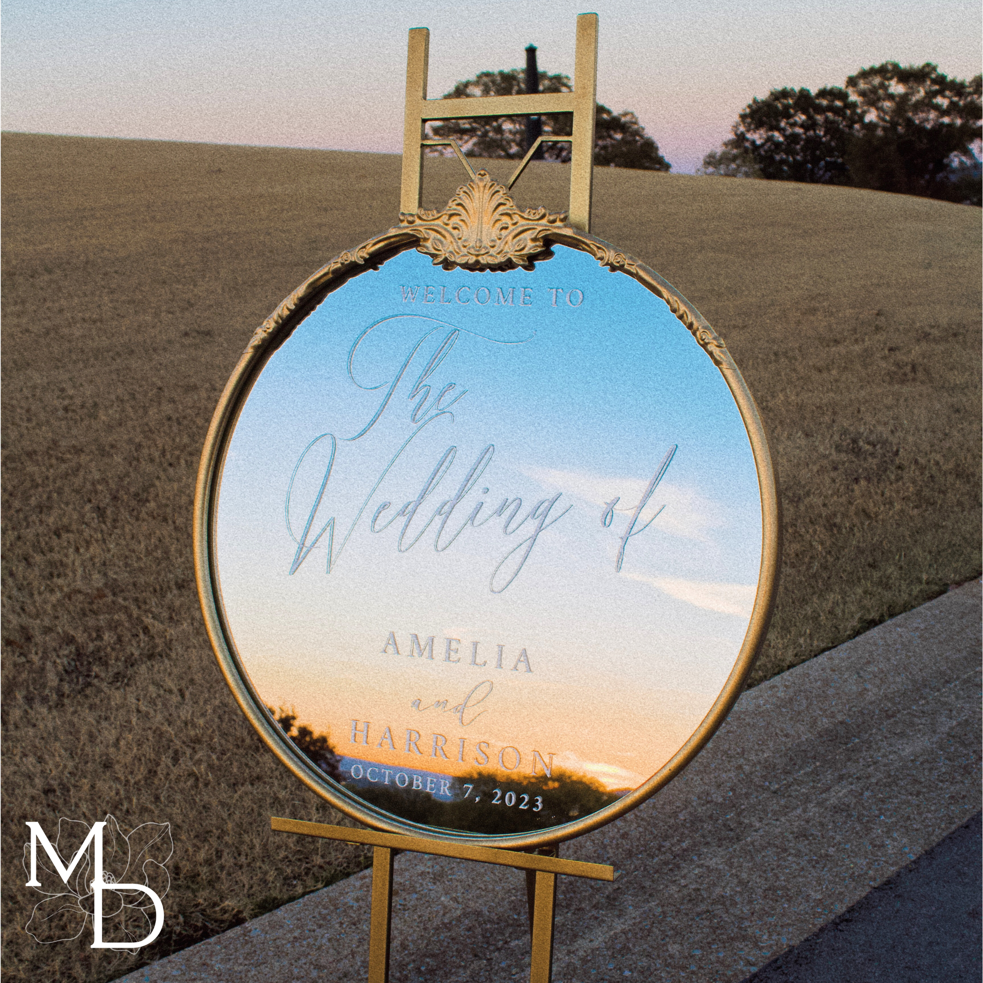 Gold ornate round mirror customized wedding welcome sign on easel outdoors.