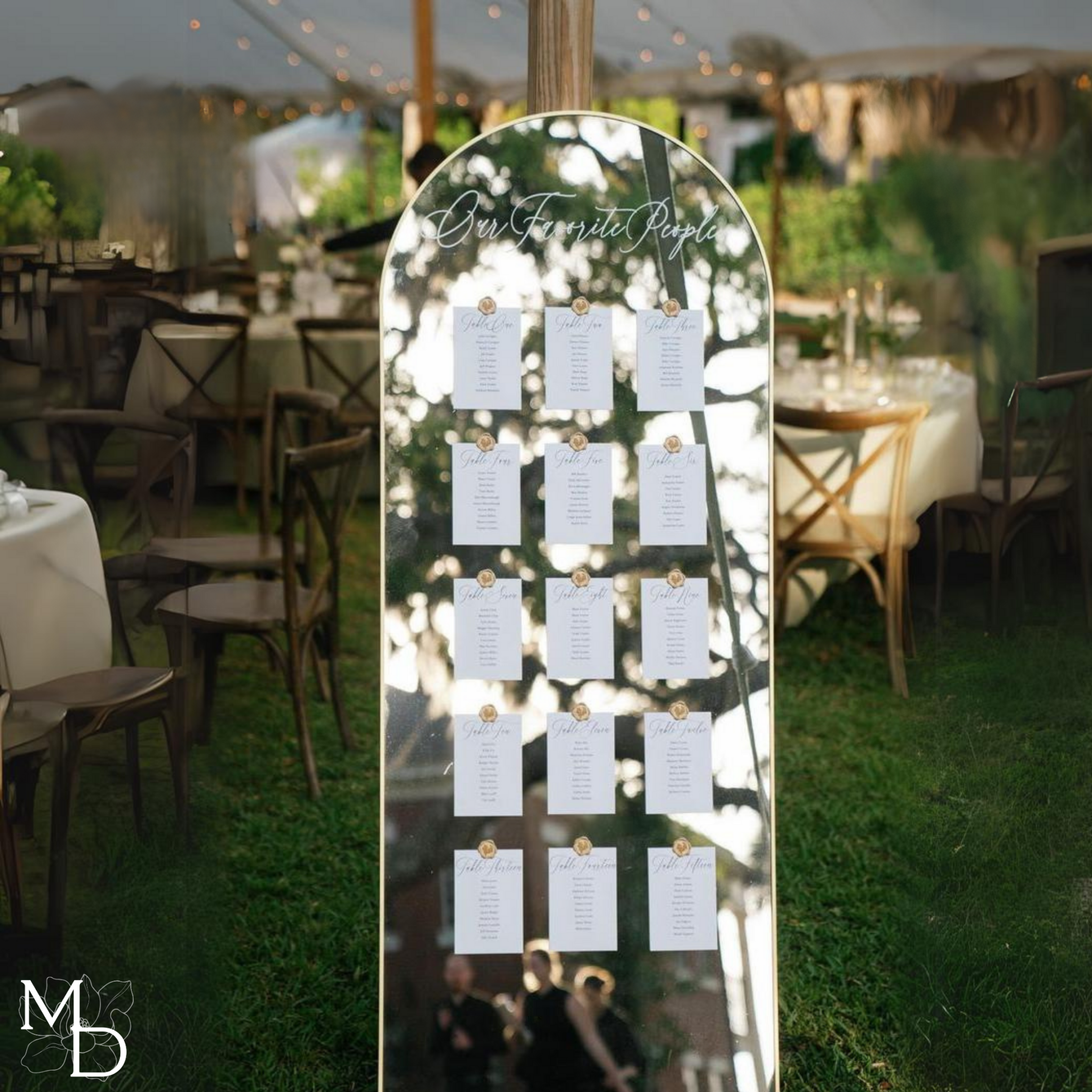 Large gold arch mirror wedding table seating chart at outdoor reception.