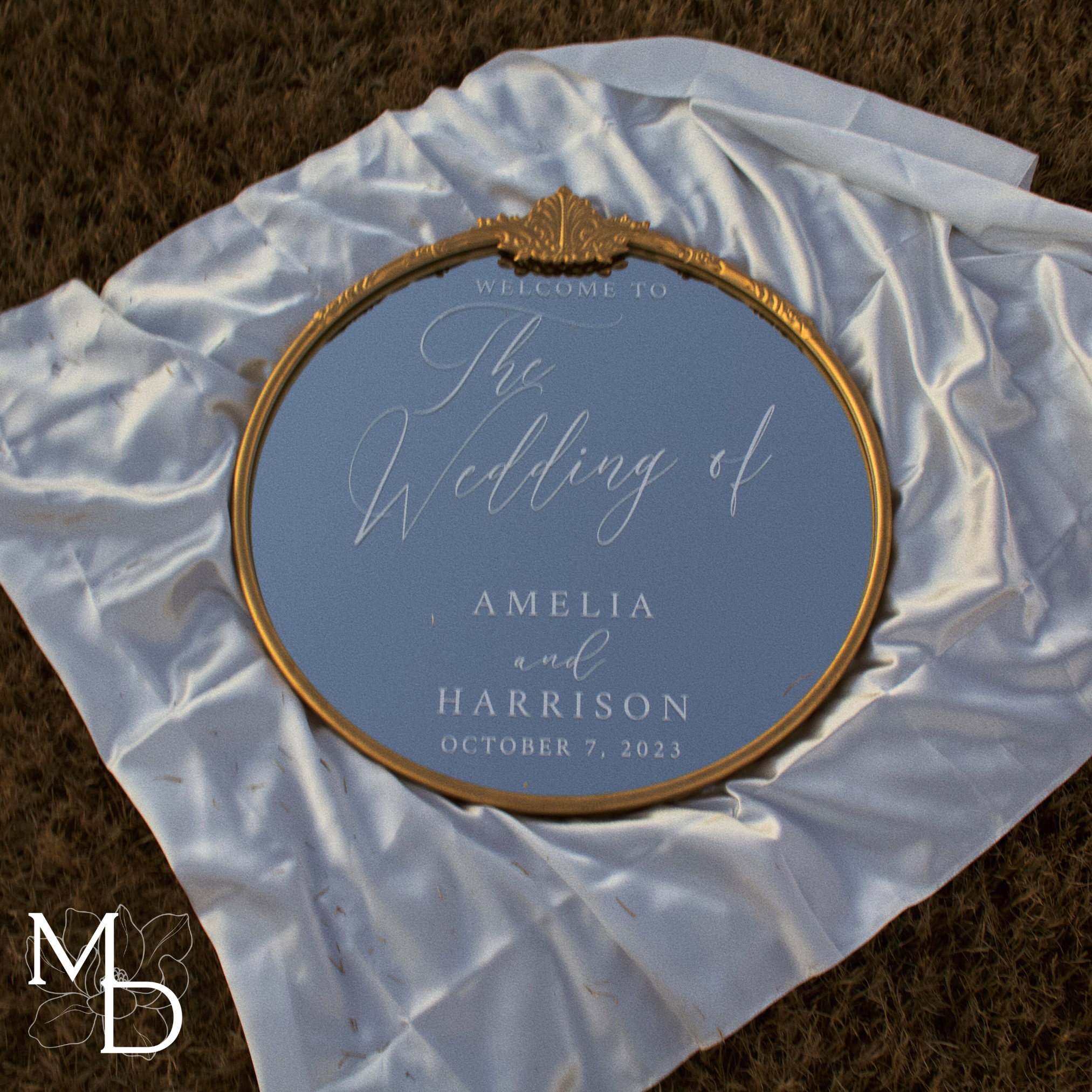 Gold ornate round mirror customized wedding welcome sign on white fabric.