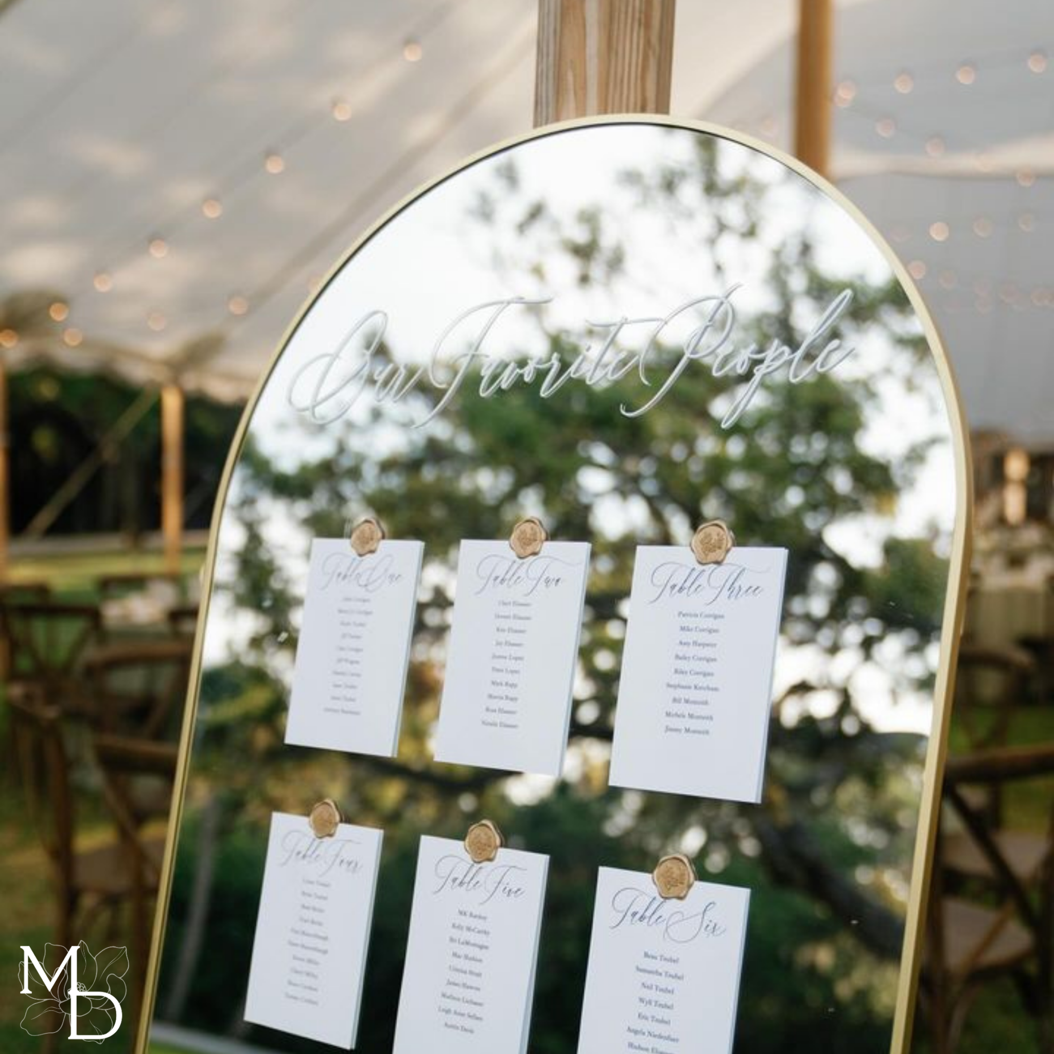 Large gold arch mirror with wedding table seating chart displayed on linen cardstock, personalized for wedding reception.