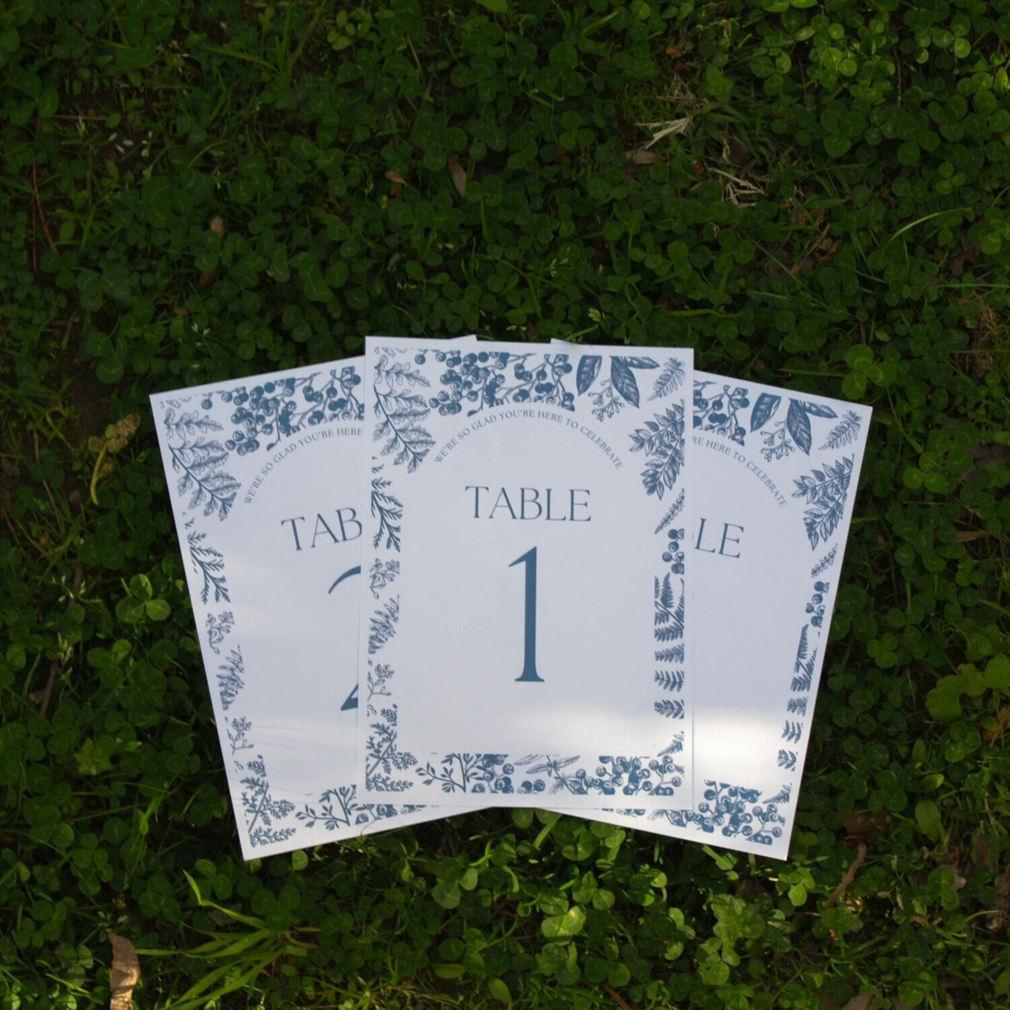 Blue & white wedding table numbers on linen cardstock displayed on grass.