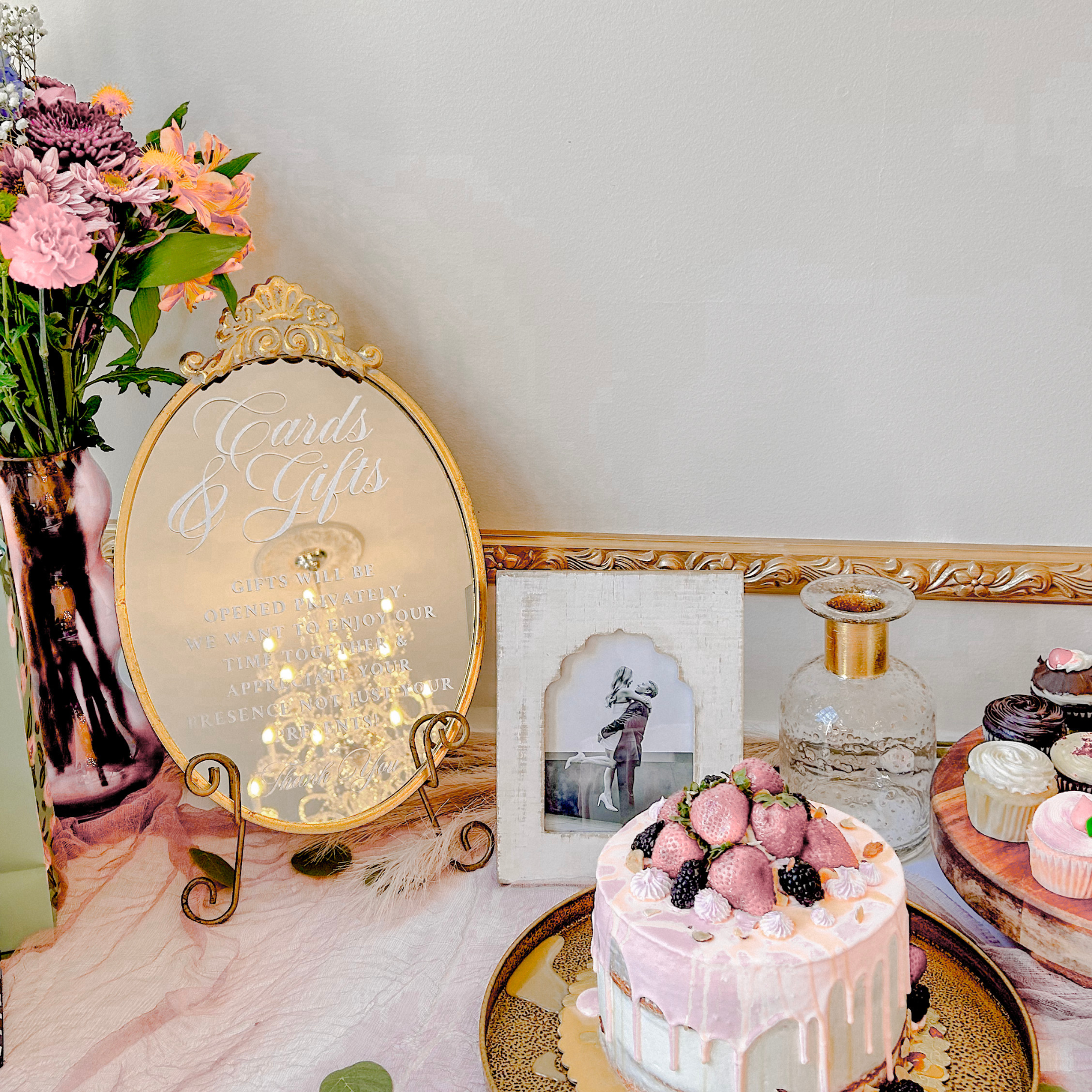 Elegant mirror wedding sign for cards and gifts table with ornate gold design, surrounded by flowers and desserts.