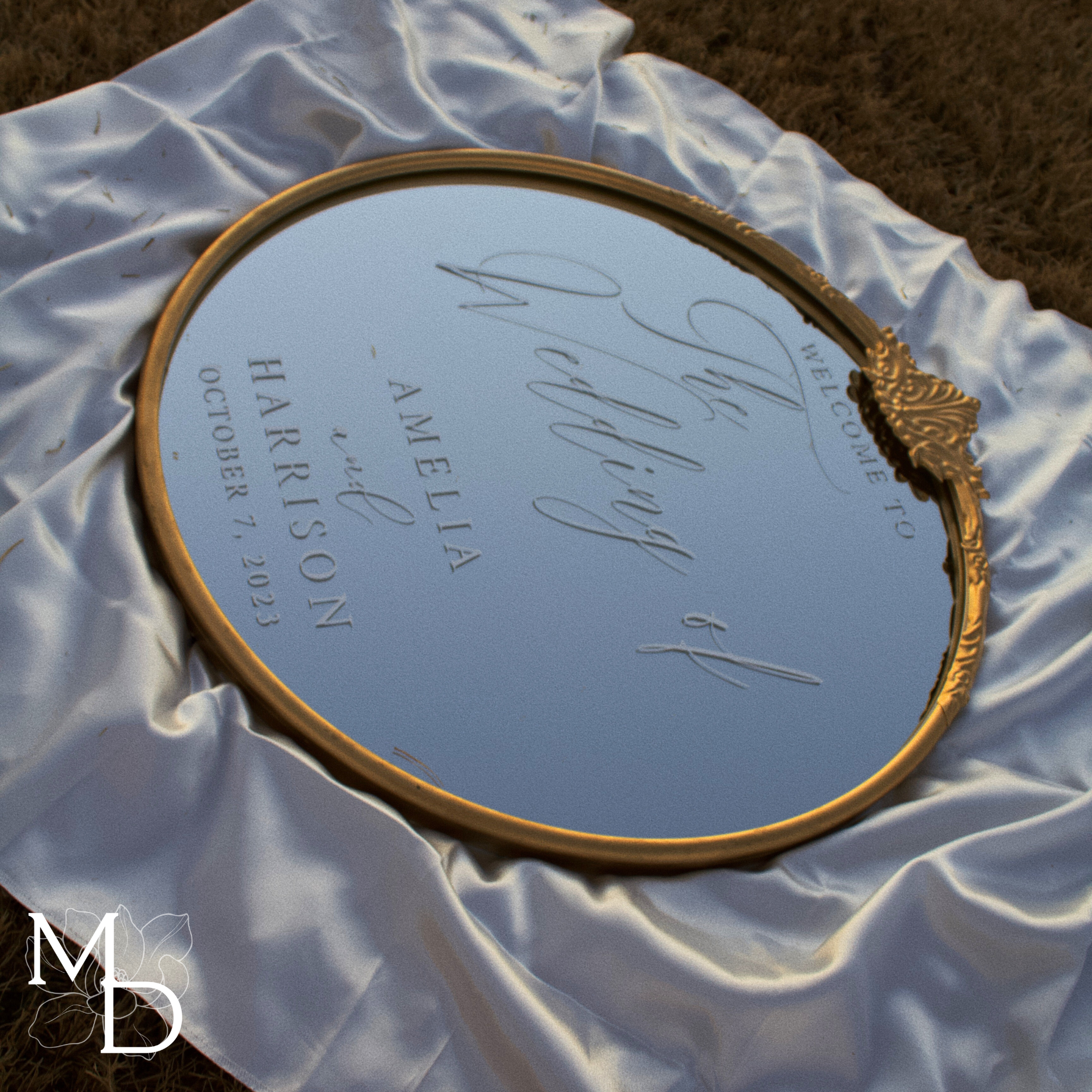 Gold ornate round mirror customized wedding welcome sign on white fabric.