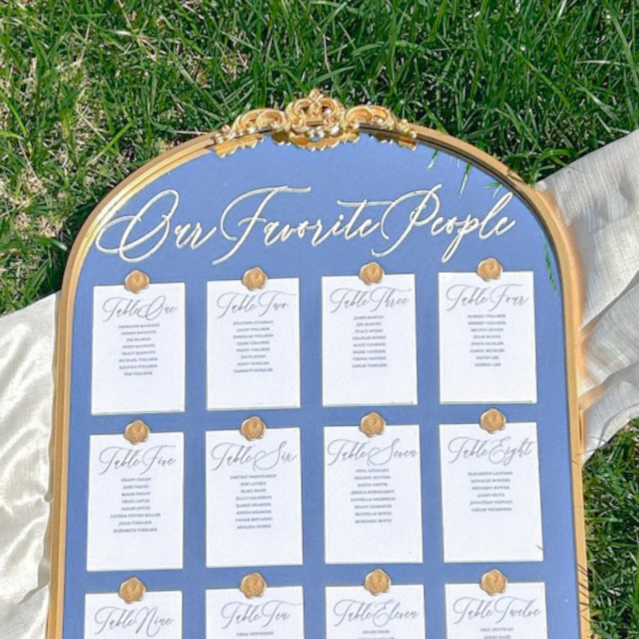 Wedding seating chart with "Our Favorite People" vinyl decal, featuring a gold-trimmed blue board on grass.