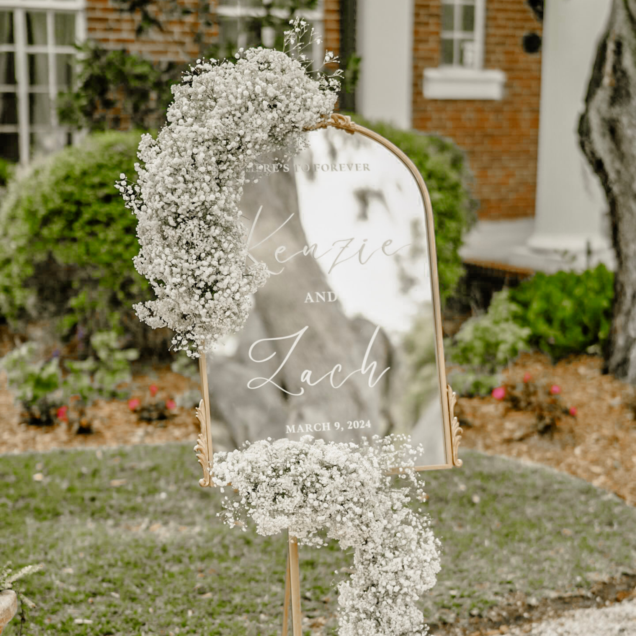 Personalized gold mirror welcome sign adorned with flowers for engagement party and wedding reception.