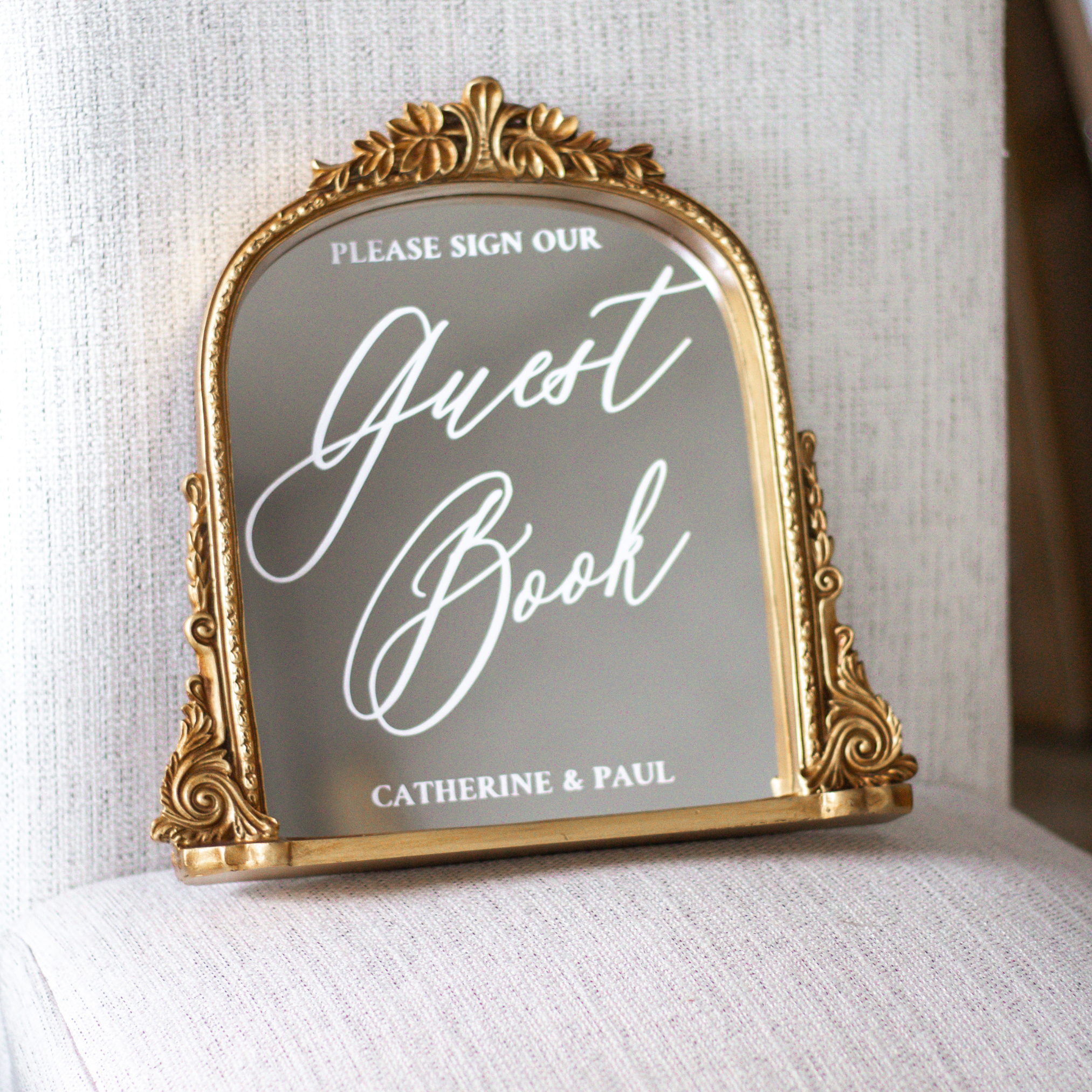 Elegant wedding guest book sign with gold ornate frame on chair.