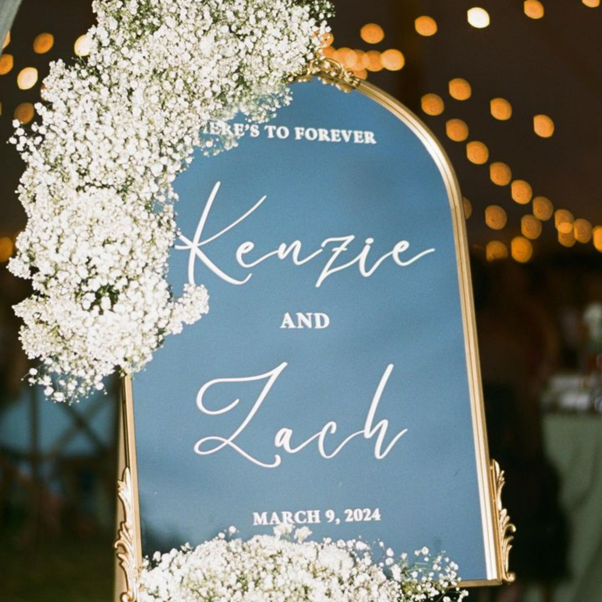 Personalized gold mirror welcome sign for engagement party and wedding reception with floral decoration.