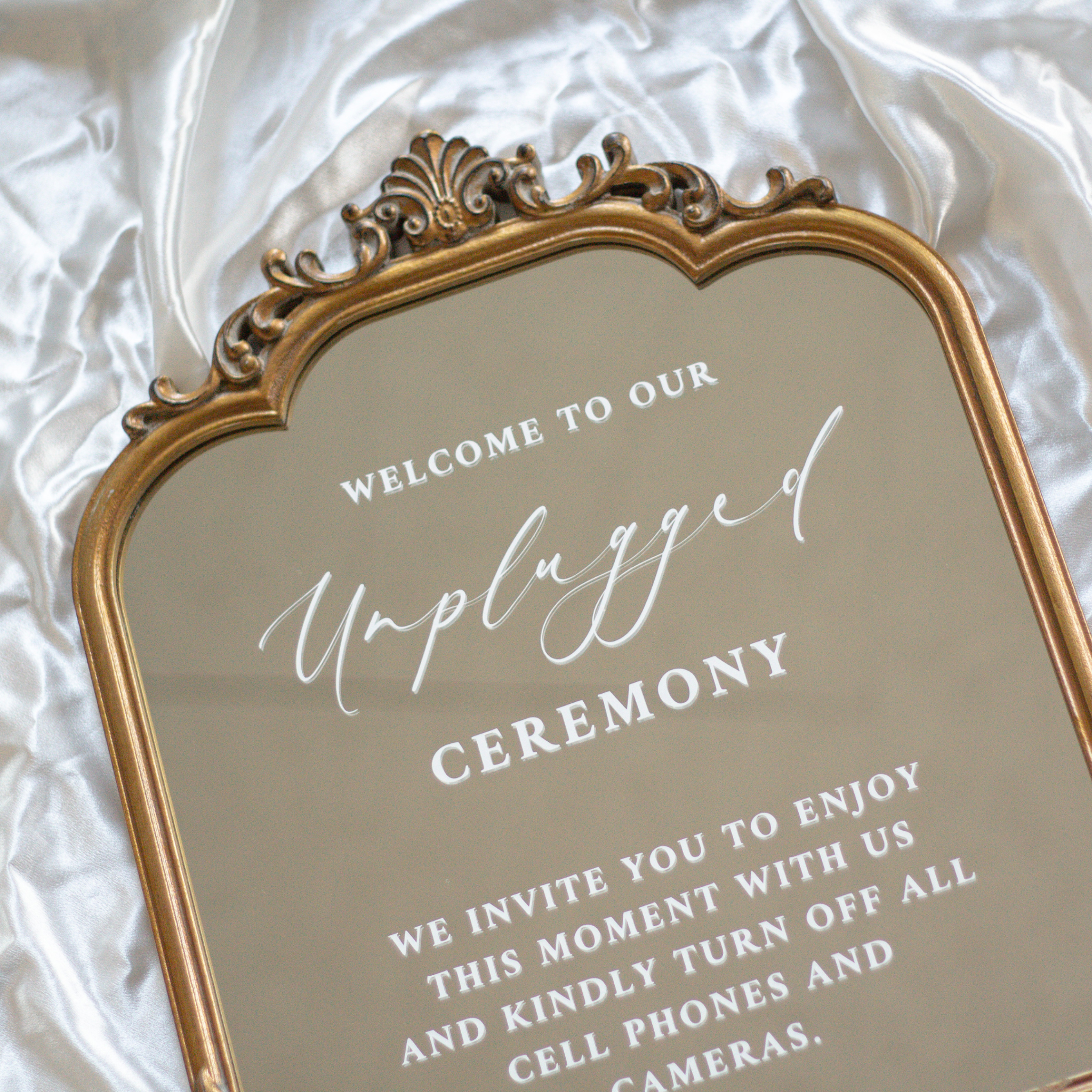 Elegant unplugged ceremony sign on a wedding mirror promoting phone-free etiquette.