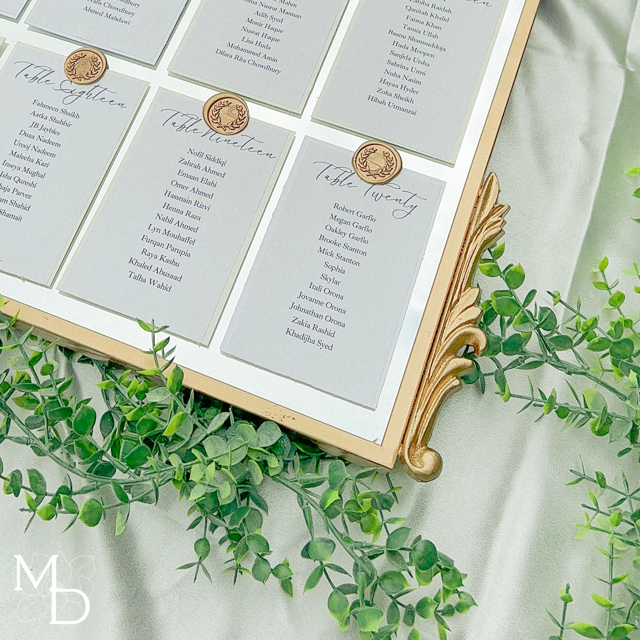 Elegant wedding guest table layout on gold arch mirror with customized vinyl decal and wax seals.